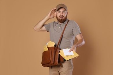 Emotional young postman with leather bag delivering letters on brown background