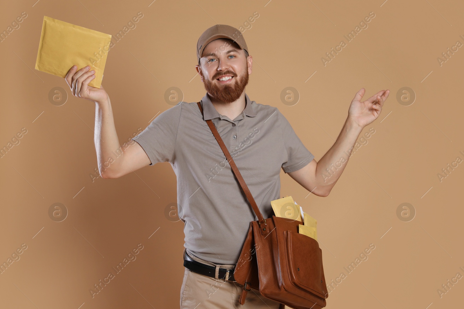 Photo of Happy young postman with leather bag delivering letters on brown background