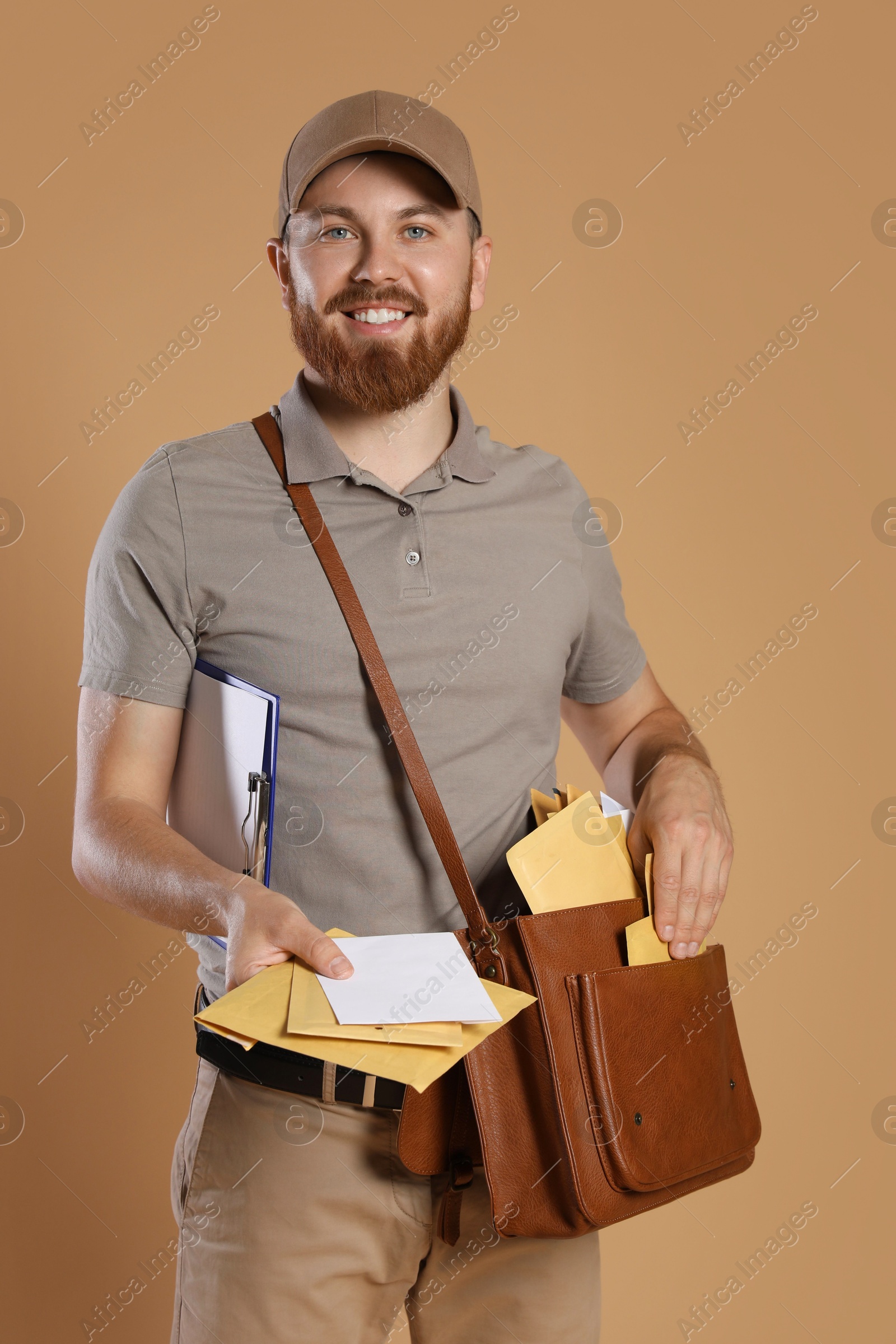 Photo of Happy young postman with leather bag delivering letters on brown background