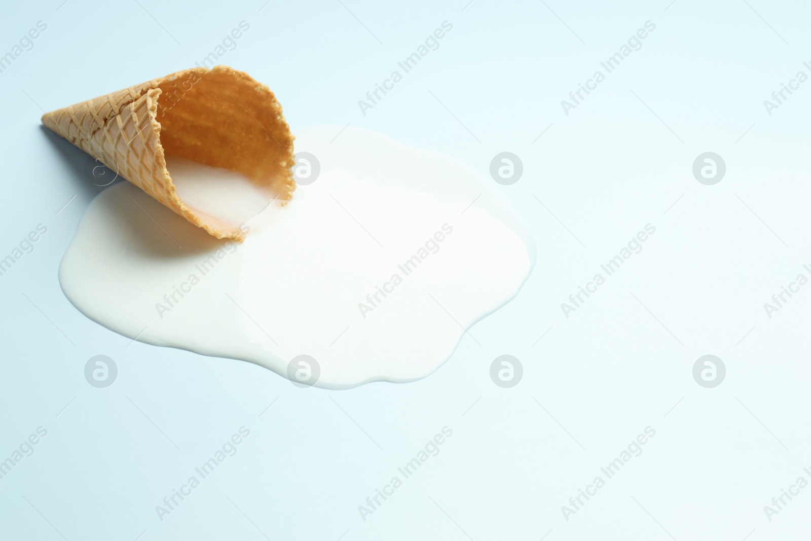 Photo of Melted ice cream and wafer cone on light background. Space for text