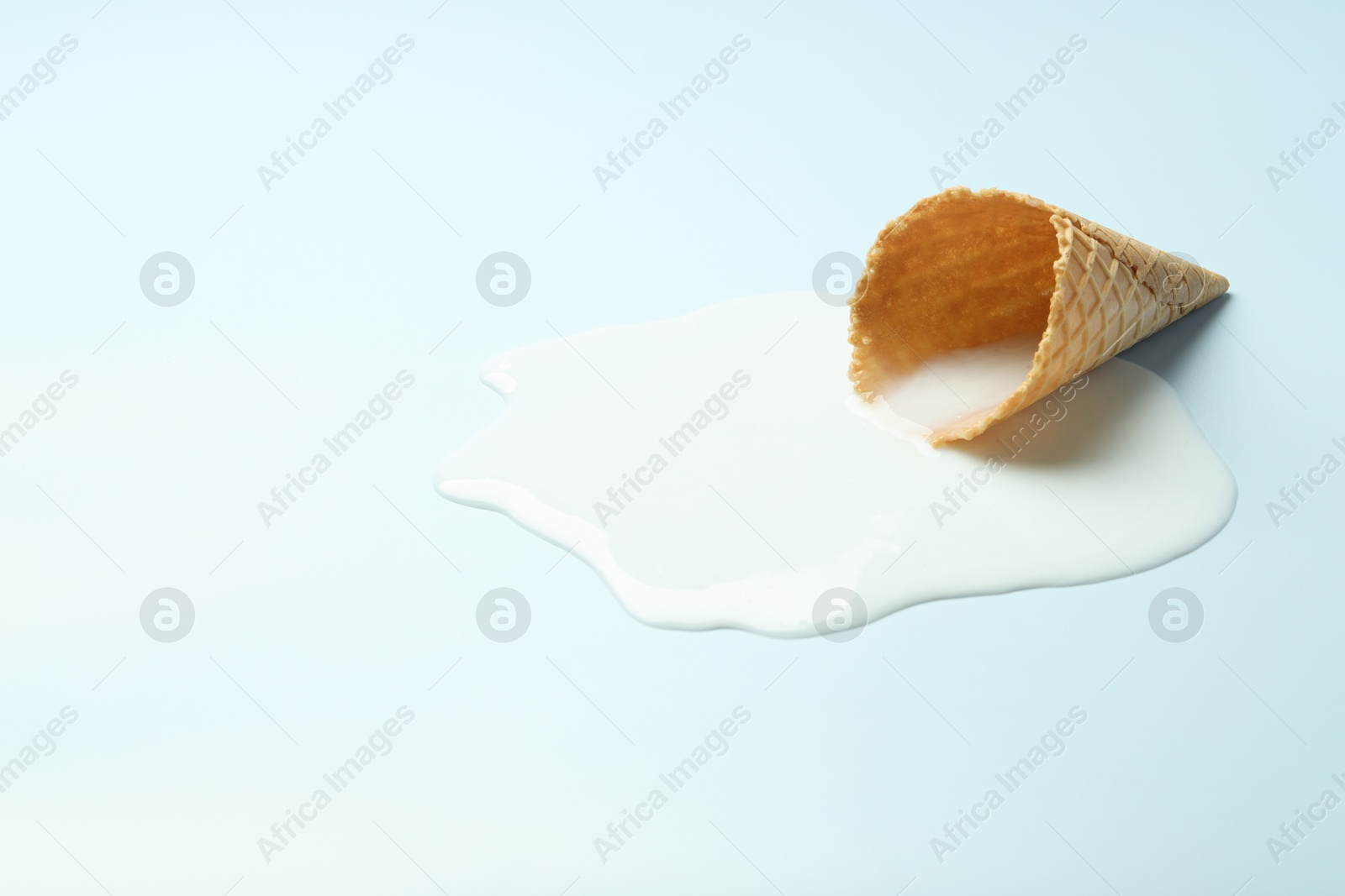 Photo of Melted ice cream and wafer cone on light background. Space for text