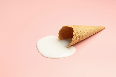 Melted ice cream and wafer cone on light pink background