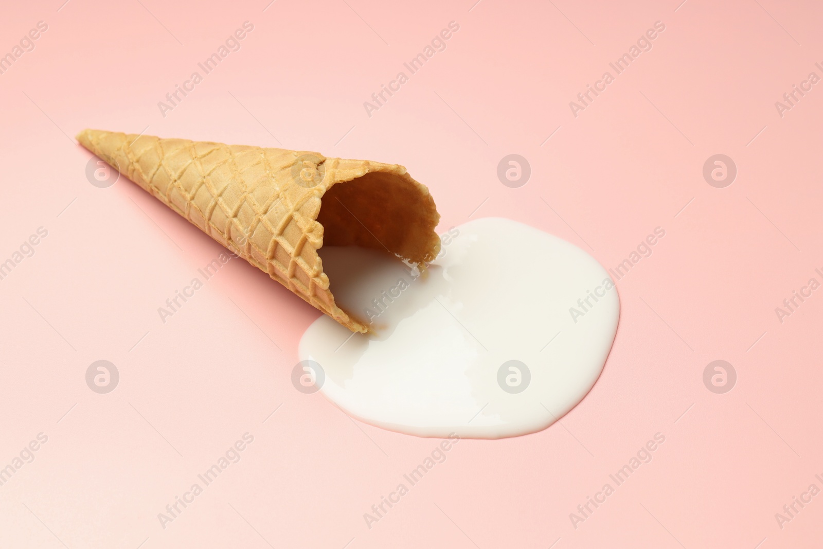 Photo of Melted ice cream and wafer cone on light pink background