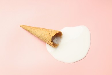 Melted ice cream and wafer cone on light pink background, top view