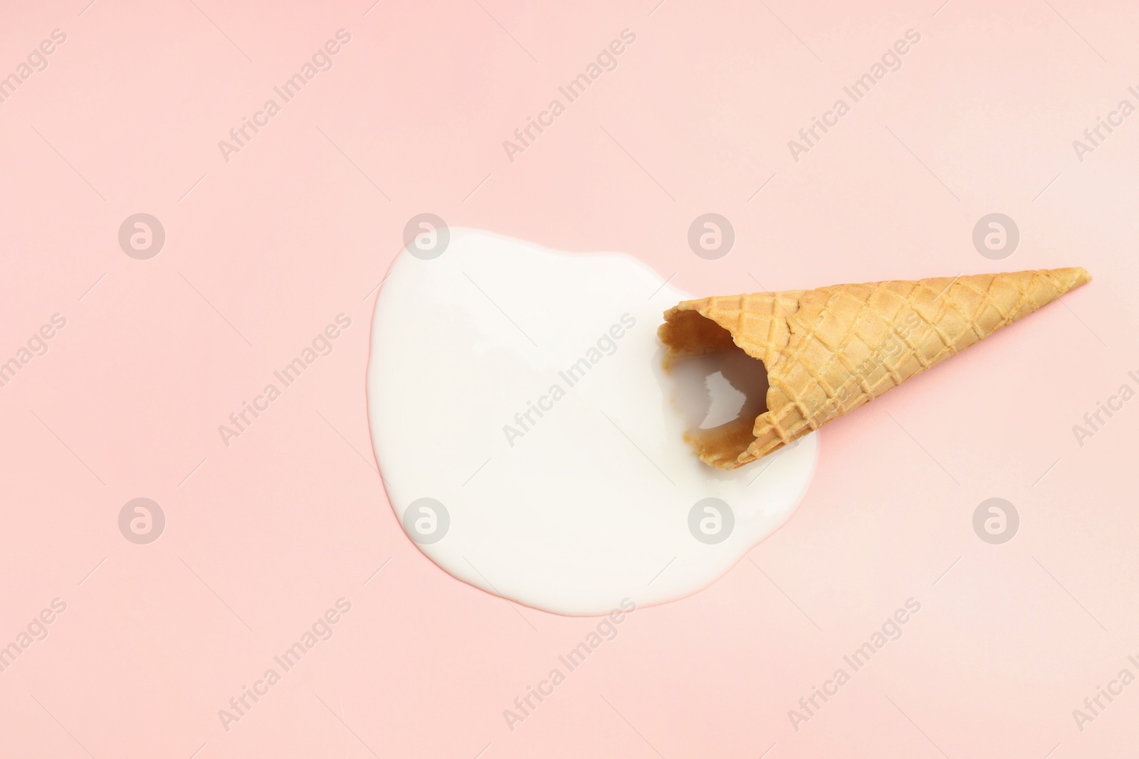 Photo of Melted ice cream and wafer cone on light pink background, top view. Space for text