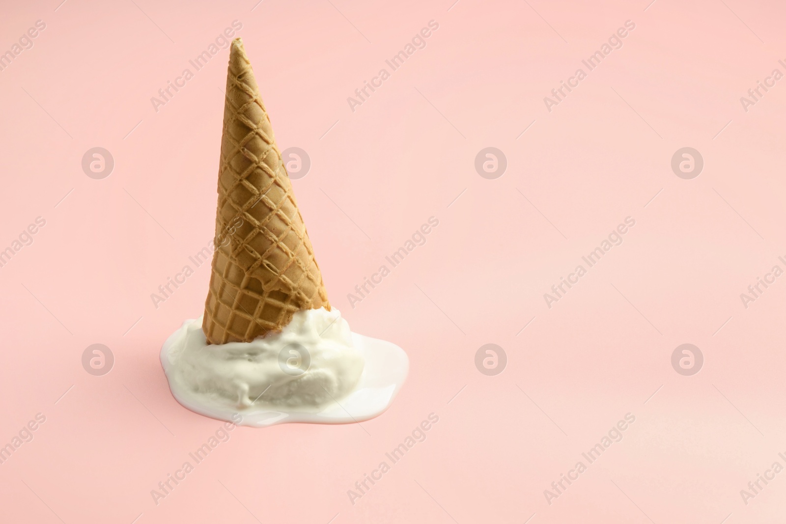 Photo of Melted ice cream in wafer cone on light pink background. Space for text