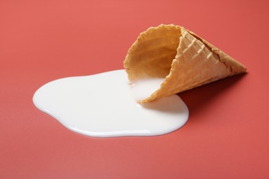 Melted ice cream and wafer cone on pale pink background