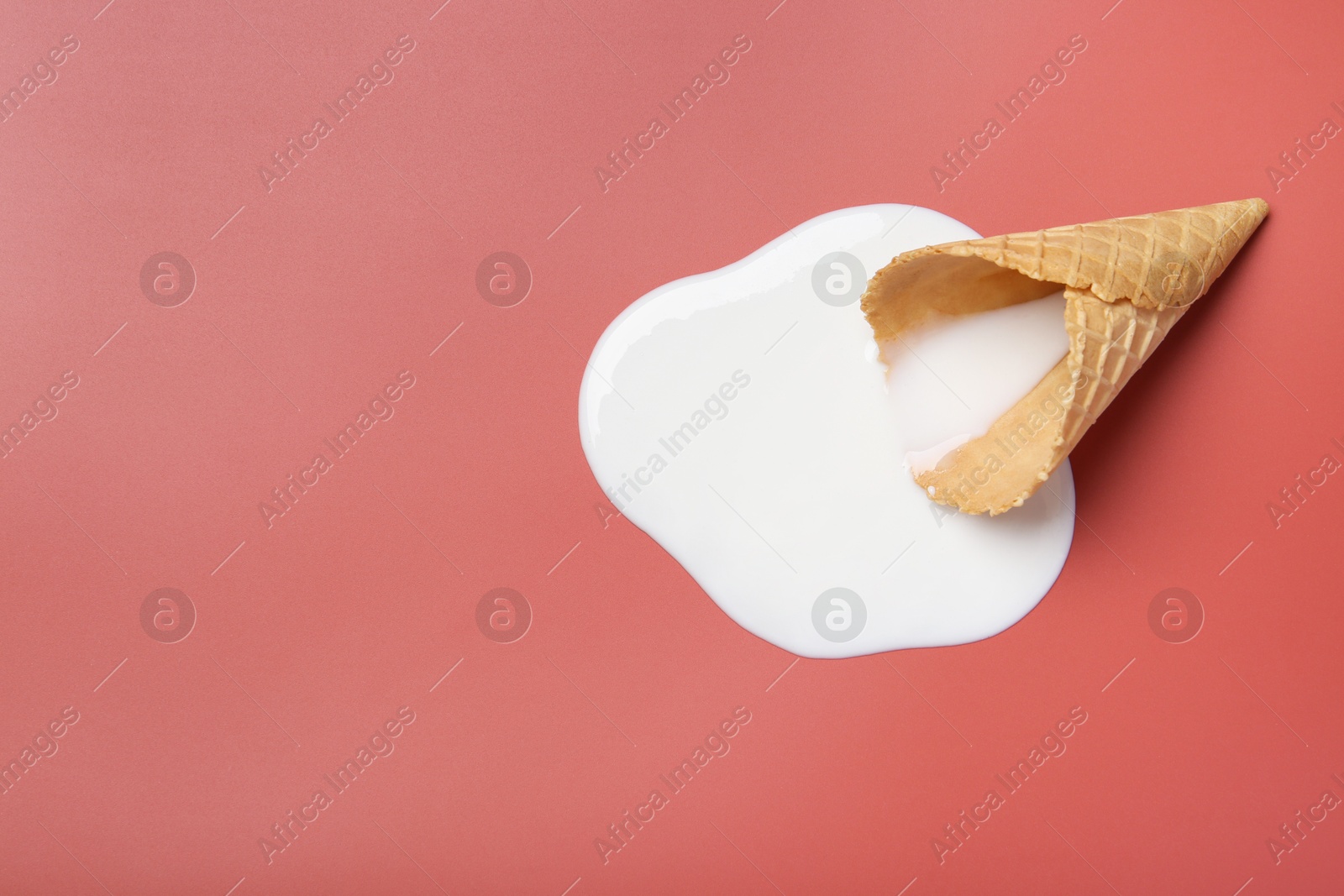 Photo of Melted ice cream and wafer cone on pale pink background, top view. Space for text