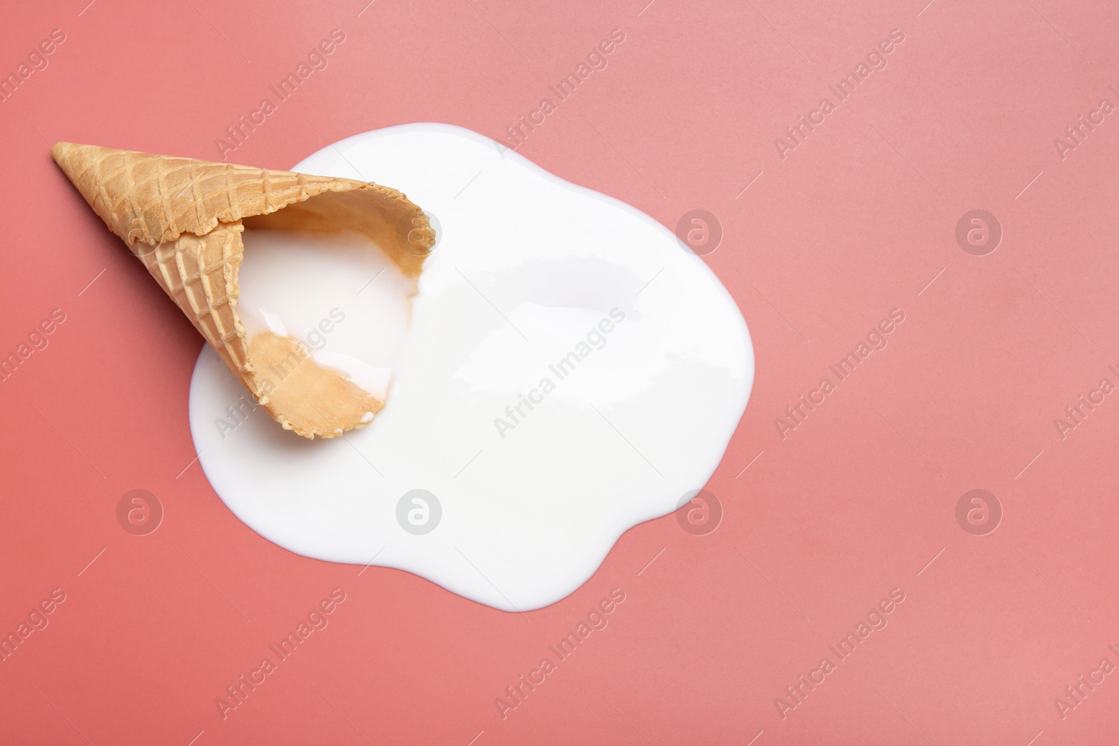 Photo of Melted ice cream and wafer cone on pale pink background, top view. Space for text