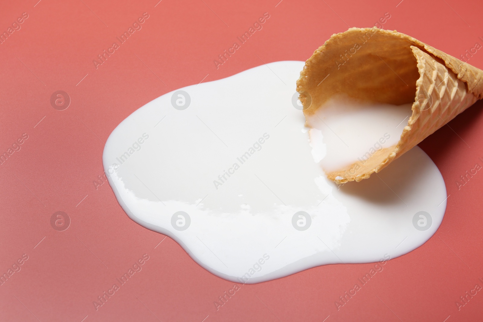 Photo of Melted ice cream and wafer cone on pale pink background, closeup