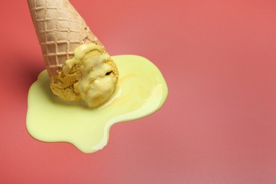 Photo of Melted ice cream in wafer cone on pale pink background, closeup. Space for text