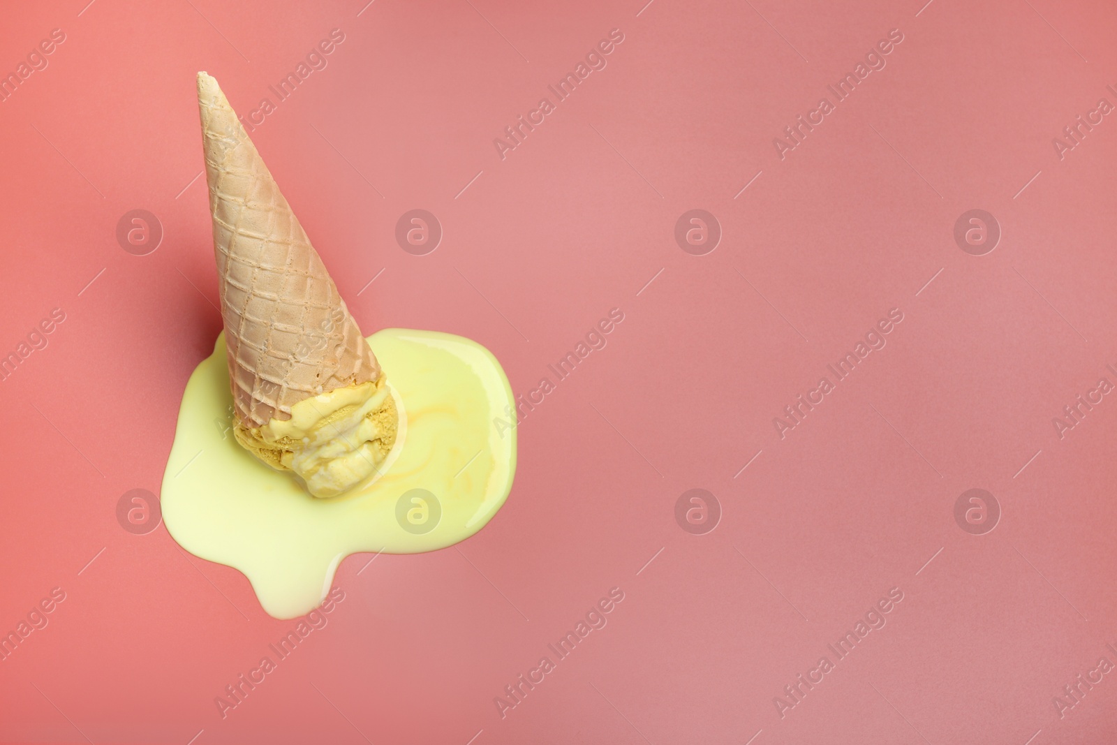 Photo of Melted ice cream in wafer cone on pale pink background. Space for text