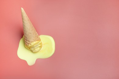 Melted ice cream in wafer cone on pale pink background. Space for text