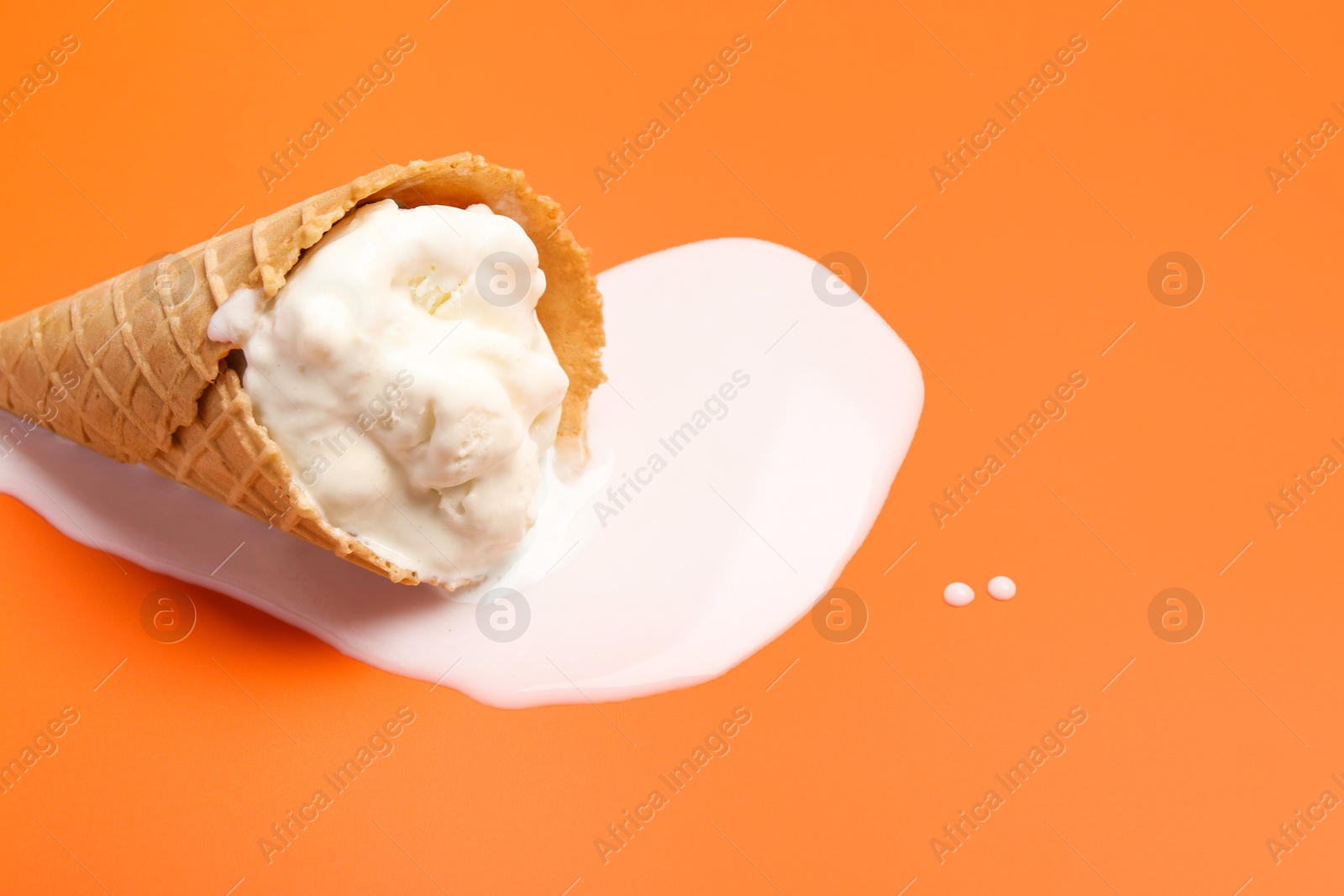 Photo of Melted ice cream in wafer cone on orange background. Space for text