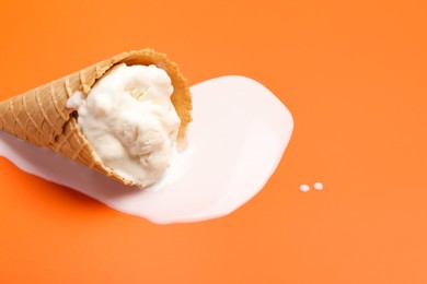 Melted ice cream in wafer cone on orange background. Space for text