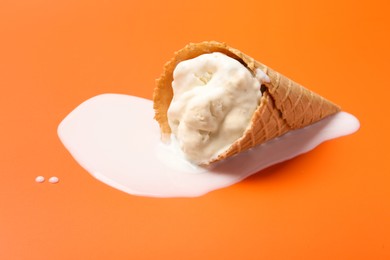 Melted ice cream in wafer cone on orange background