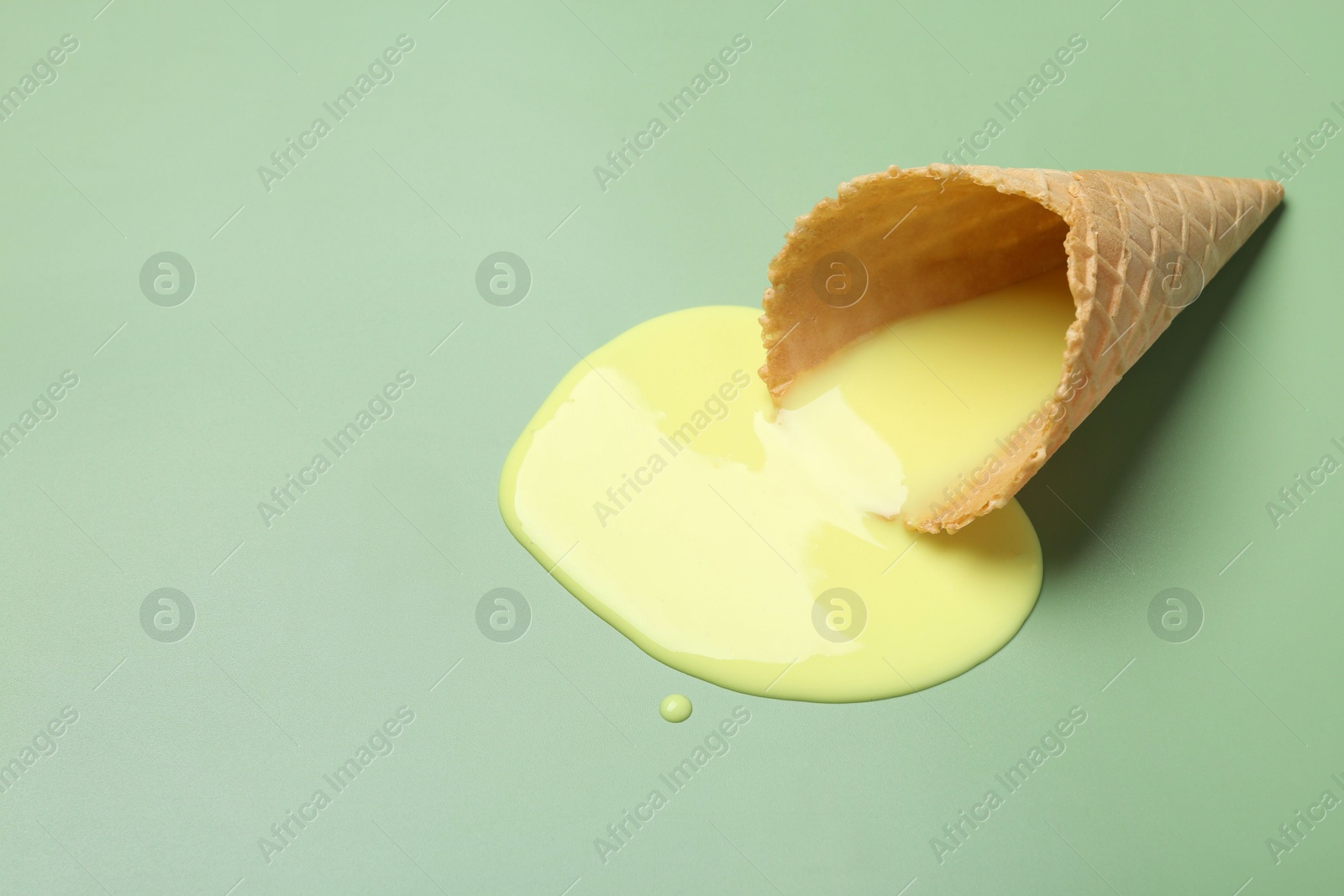 Photo of Melted ice cream and wafer cone on light green background. Space for text