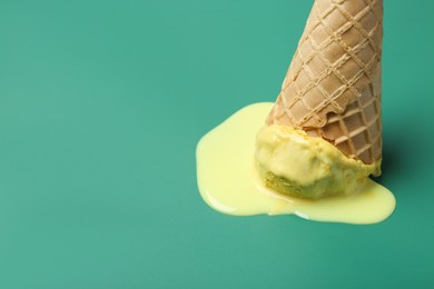 Photo of Melted ice cream in wafer cone on pale green background, closeup. Space for text