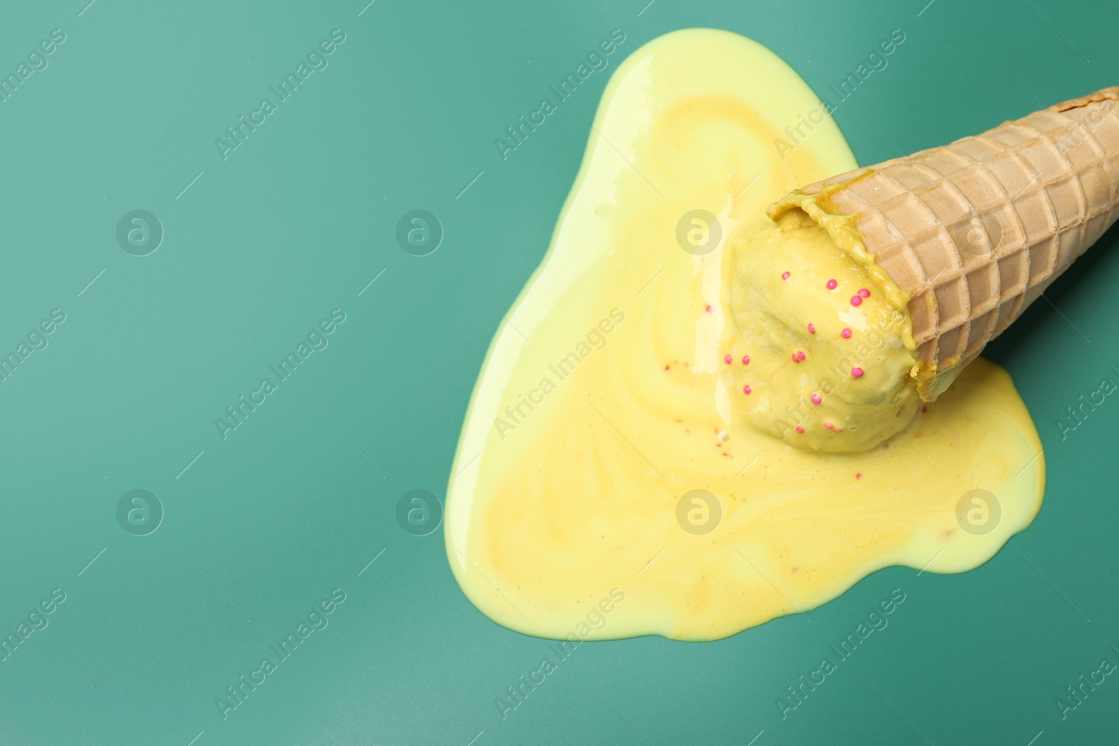 Photo of Melted ice cream in wafer cone on pale green background, top view. Space for text