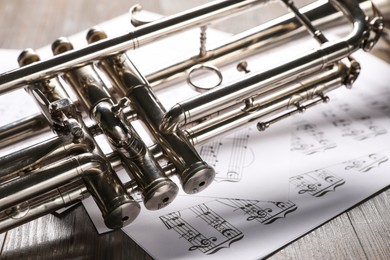 Trumpet and music sheet papers with notes on wooden table, closeup