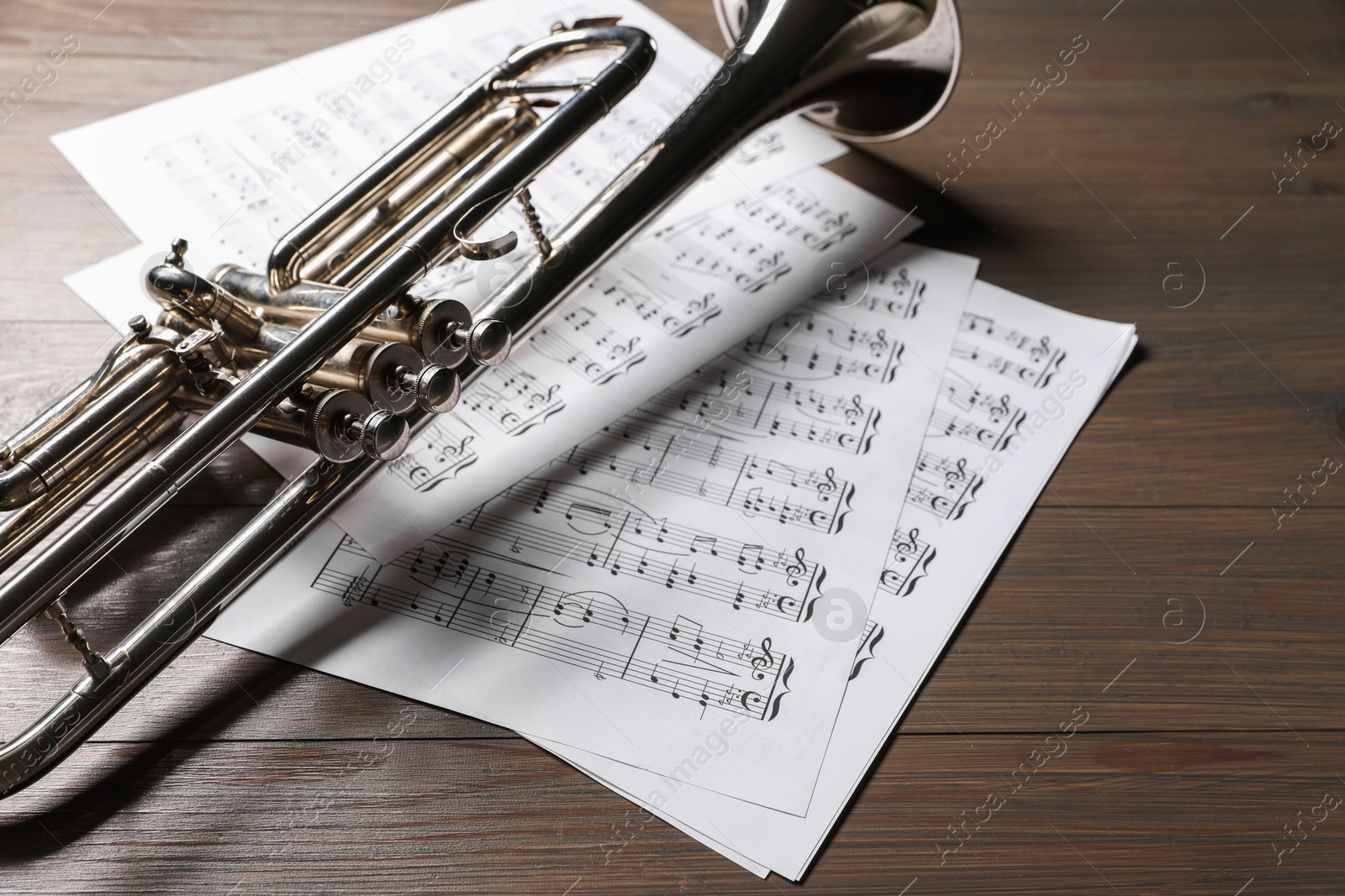 Photo of Trumpet and music sheet papers with notes on wooden table, closeup