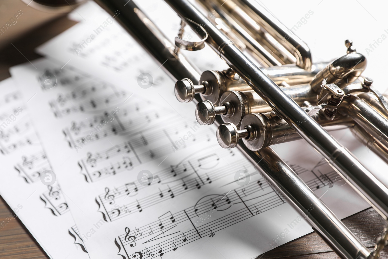 Photo of Trumpet and music sheet papers with notes on wooden table, closeup