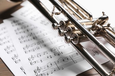 Photo of Trumpet and music sheet papers with notes on wooden table, closeup