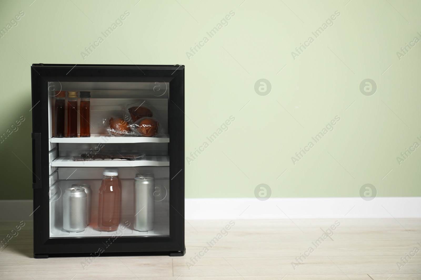 Photo of Mini refrigerator with different drinks and snacks near olive wall, space for text