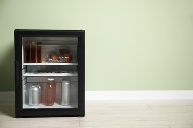 Photo of Mini refrigerator with different drinks and snacks near olive wall, space for text