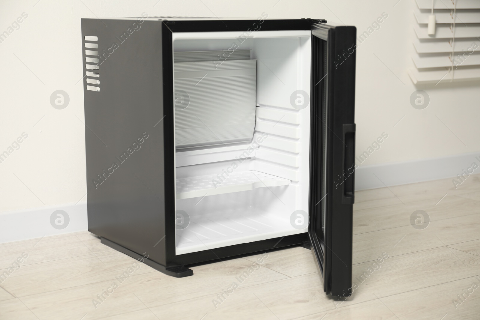 Photo of Empty modern mini refrigerator near white wall