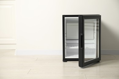 Empty modern mini refrigerator near white wall, space for text