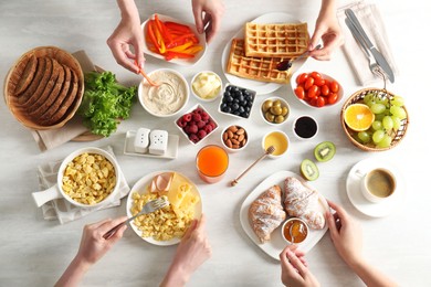 Photo of Women having tasty breakfast at light wooden table, top view