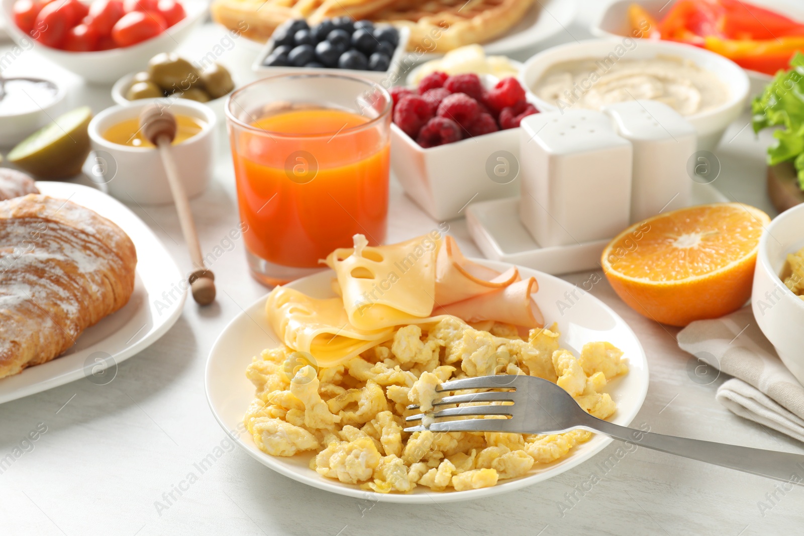 Photo of Tasty breakfast. Scrambled eggs, ham, cheese and other food served on light wooden table, closeup