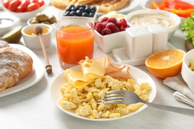 Photo of Tasty breakfast. Scrambled eggs, ham, cheese and other food served on light wooden table, closeup