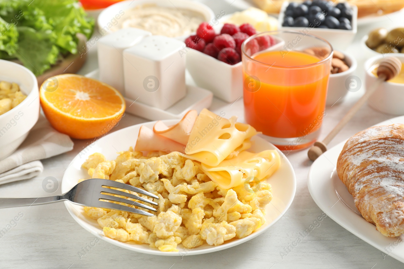 Photo of Tasty breakfast. Scrambled eggs, ham, cheese and other food served on light wooden table, closeup