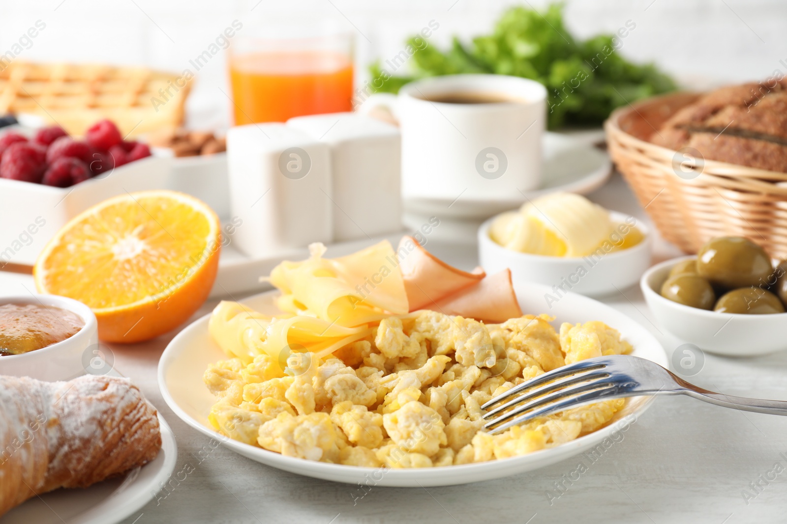 Photo of Tasty breakfast. Scrambled eggs, ham, cheese and other food served on light table, closeup