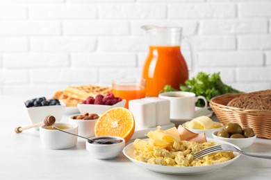 Photo of Tasty breakfast. Scrambled eggs, ham, cheese and other food served on light table