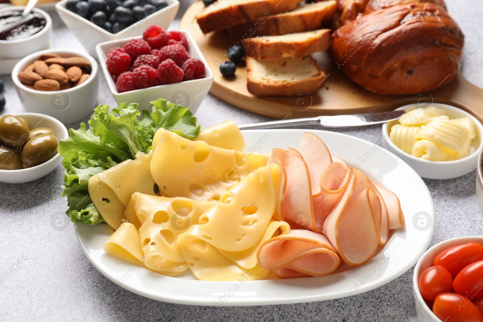 Photo of Tasty breakfast. Slices of ham, cheese, lettuce and other food on grey textured table, closeup