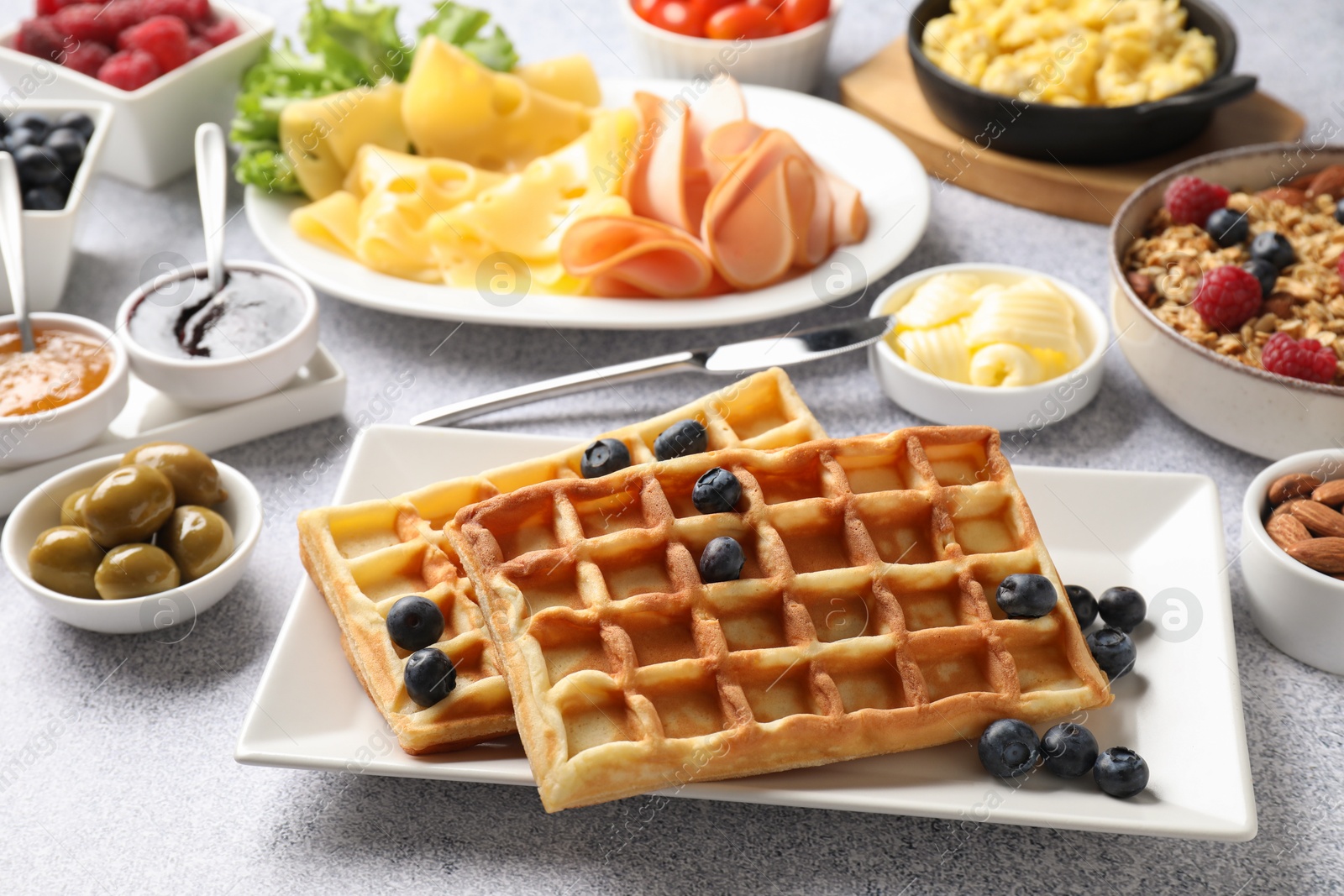 Photo of Tasty breakfast. Belgian waffles, blueberries and other food on grey textured table, closeup