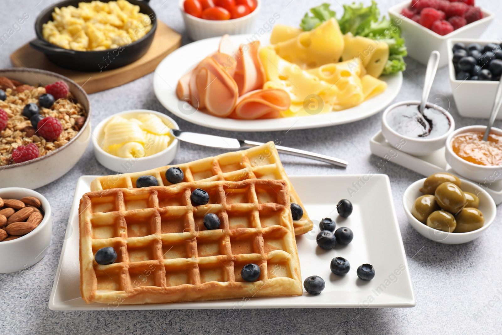 Photo of Tasty breakfast. Belgian waffles, blueberries and other food on grey textured table, closeup