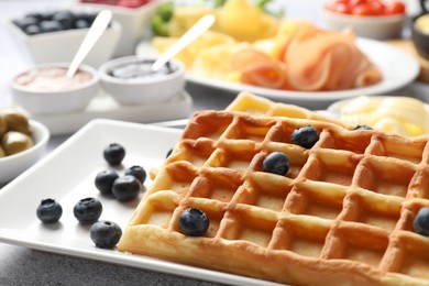 Photo of Tasty breakfast. Belgian waffles, blueberries and other food on grey textured table, closeup