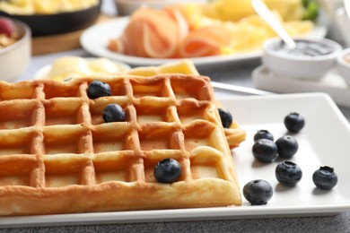 Photo of Tasty breakfast. Belgian waffles, blueberries and other food on grey textured table, closeup