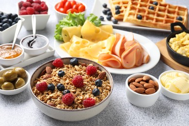 Photo of Tasty breakfast. Granola with berries and other food on grey textured table, closeup