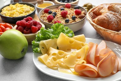 Photo of Tasty breakfast. Slices of ham, cheese, lettuce, apple and other food on grey textured table, closeup