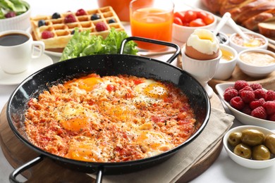 Tasty shakshouka in frying pan and other meals served for breakfast on white table, closeup