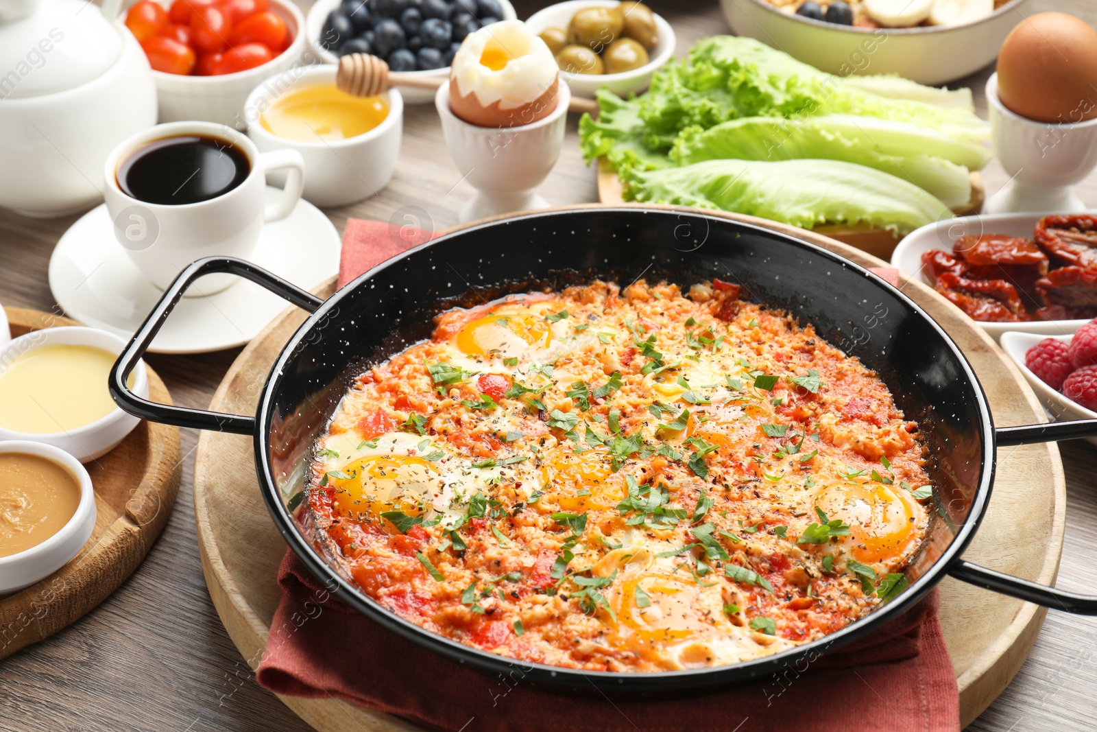 Photo of Tasty shakshouka in frying pan and other meals served for breakfast on wooden table