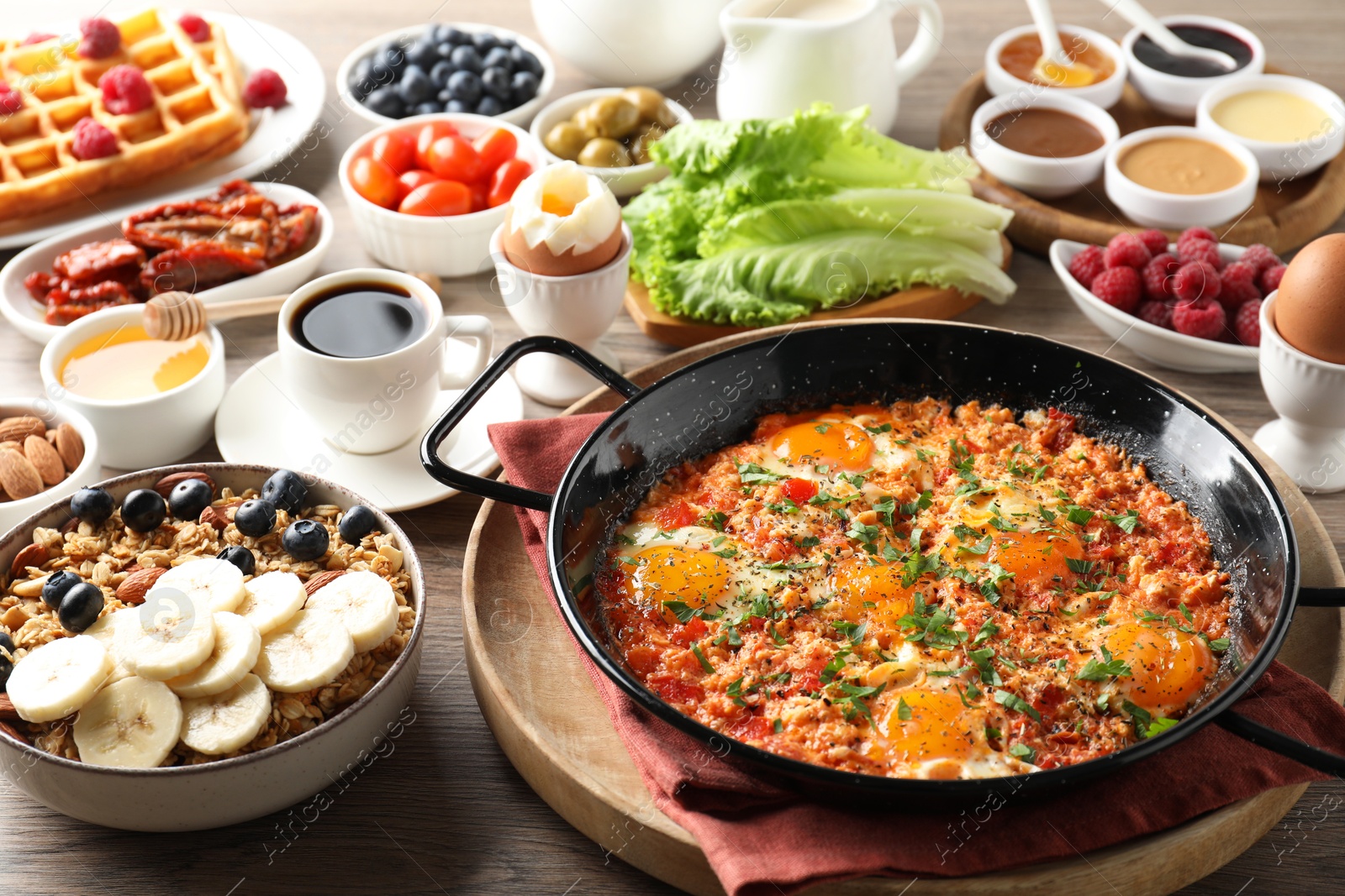 Photo of Tasty shakshouka in frying pan and other meals served for breakfast on wooden table