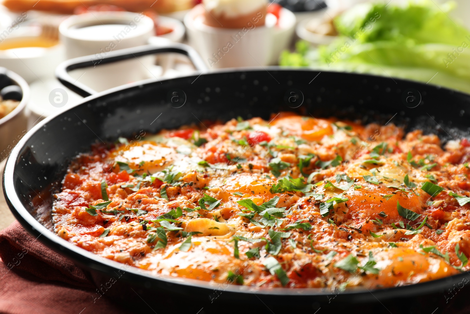 Photo of Tasty shakshouka in frying pan served for breakfast on wooden table, closeup