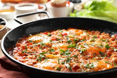 Tasty shakshouka in frying pan served for breakfast on wooden table, closeup