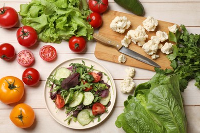 Healthy vegetarian food. Plate of salad and vegetables on light wooden table, flat lay